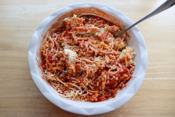Salsa, shredded cheese, cream cheese and diced green onion mixed together in a large white circular baking dish.