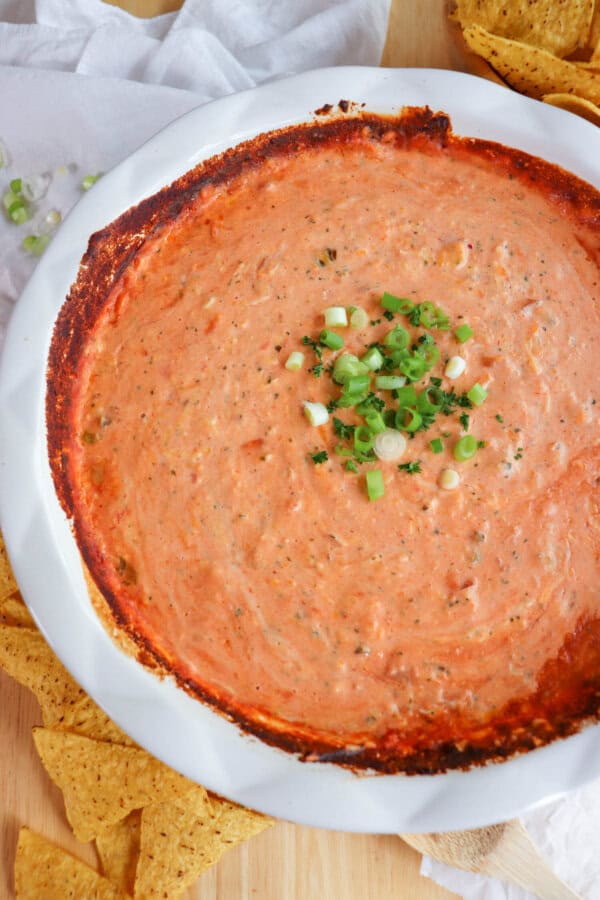 Creamy dip made from salsa and cheese in a white baking dished topped with diced green onions in the center surrounded by tortilla chips.