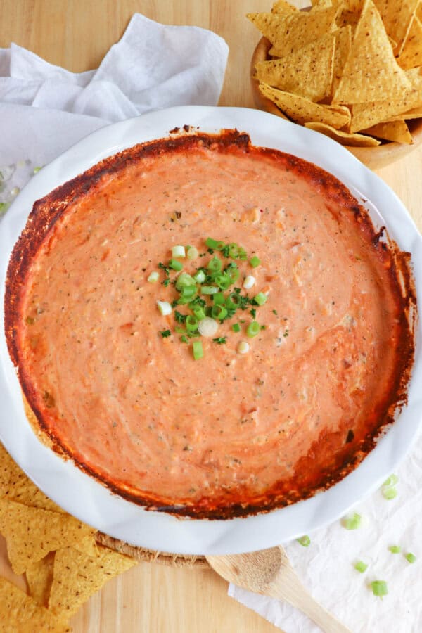 Creamy dip made from salsa and cheese in a white baking dished topped with diced green onions in the center and surrounded by tortilla chips.