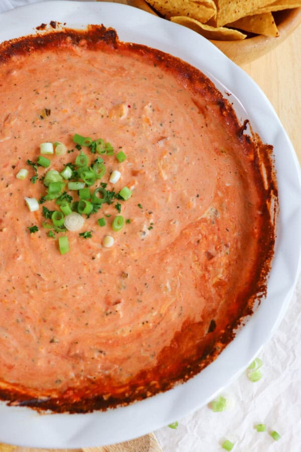 Creamy dip made from salsa and cheese in a white baking dished topped with diced green onions in the center.