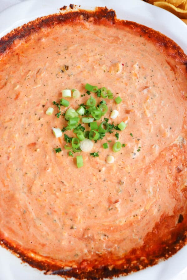 Creamy dip made from salsa and cheese in a white baking dished topped with diced green onions in the center.