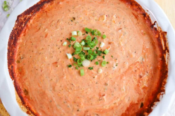 Creamy dip made from salsa and cheese in a white baking dished topped with diced green onions in the center.