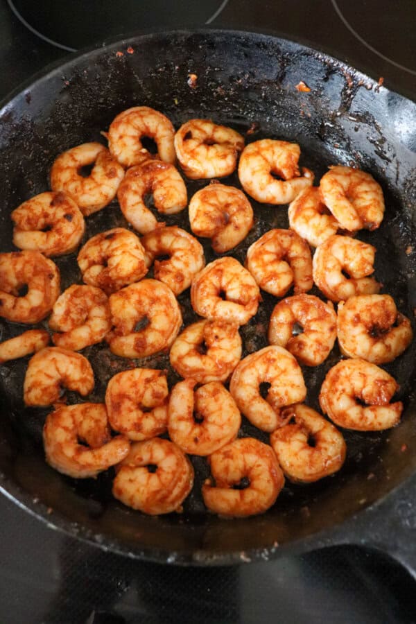 Shrimp covered in seasoning and cooked in a cast iron skillet.