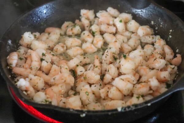 Shrimp cut into thirds cooking in a cast iron skillet on the stove top.
