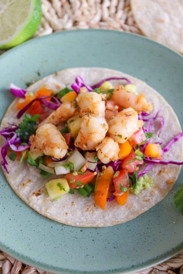 White corn tortilla on a green plate layered with red cabbage, fresh salsa and cooked shrimp.
