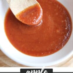Apple bourbon BBQ sauce in a small white bowl with a wooden spoon dipping into it.