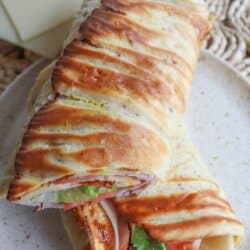 Flatbread wrap filled with lettuce, tomato, ham and cheese, cut in half diagonally and placed on a cream plate.