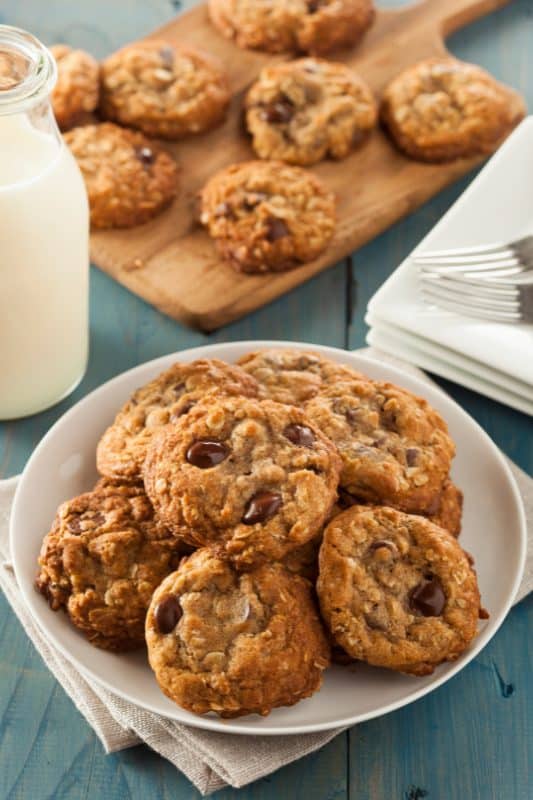 Oatmeal chocolate chip cookies stacked on a white plate with a jug of milk in the background.