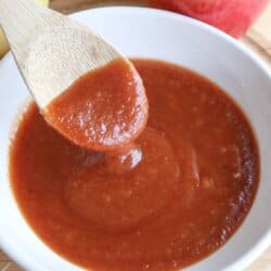 Apple bourbon BBQ sauce in a small white bowl with a wooden spoon dipping into it.