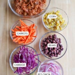 Pulled pork burrito bowl ingredients in clear glass bowls on a wooden table.