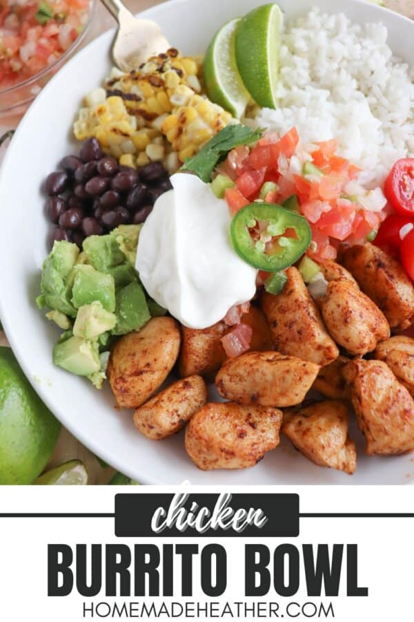 Cooked chicken bites with seasoning in a large white bowl with rice, diced avocado, black beans, corn kernels, cherry tomatoes, pico and sour cream topped with a slice of jalapeno and lime.
