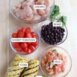 Chicken burrito bowl ingredients in clear glass bowls on a wooden table.
