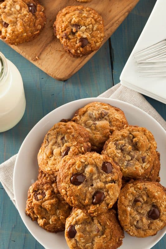 Oatmeal chocolate chip cookies stacked on a white plate with a jug of milk in the background.