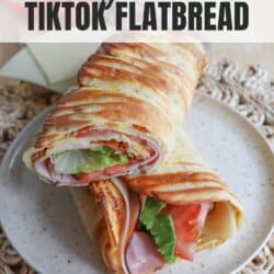 Flatbread wrap filled with lettuce, tomato, ham and cheese, cut in half diagonally and placed on a cream plate.