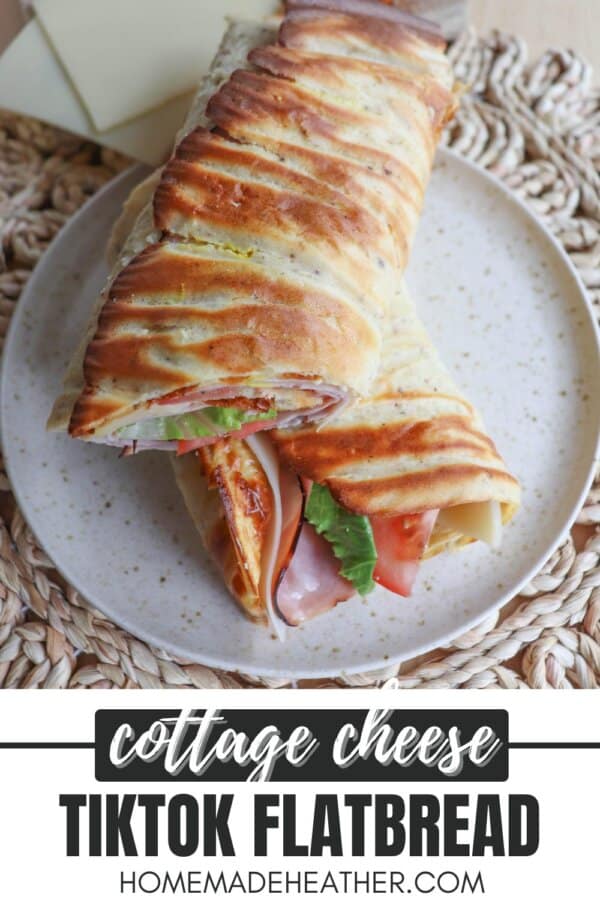 Flatbread wrap filled with lettuce, tomato, ham and cheese, cut in half diagonally and placed on a cream plate.