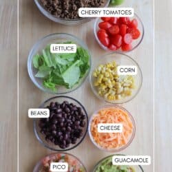Ingredients for ground beef burrito bowls in clear glass bowls on a wooden table.