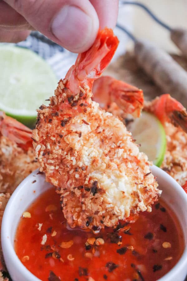 Coconut shrimp being dipped into sweet chili sauce.