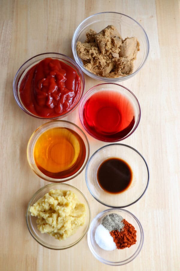 Ingredients for apple bourbon barbecue sauce in clear glass bowls on a wooden table.