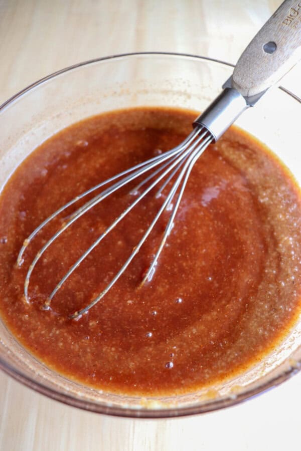 Apple bourbon BBQ sauce in a clear glass bowl with a whisk in it.
