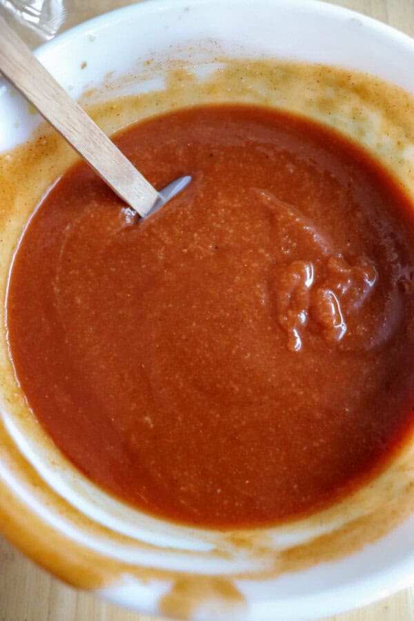 Apple bourbon BBQ sauce in a clear glass bowl with a wooden spatula in it.