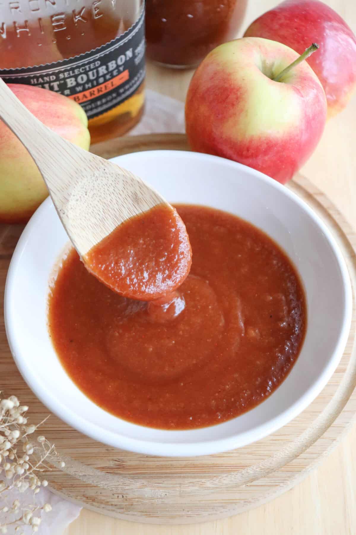 Apple bourbon BBQ sauce in a small white bowl with a wooden spoon dipping into it.