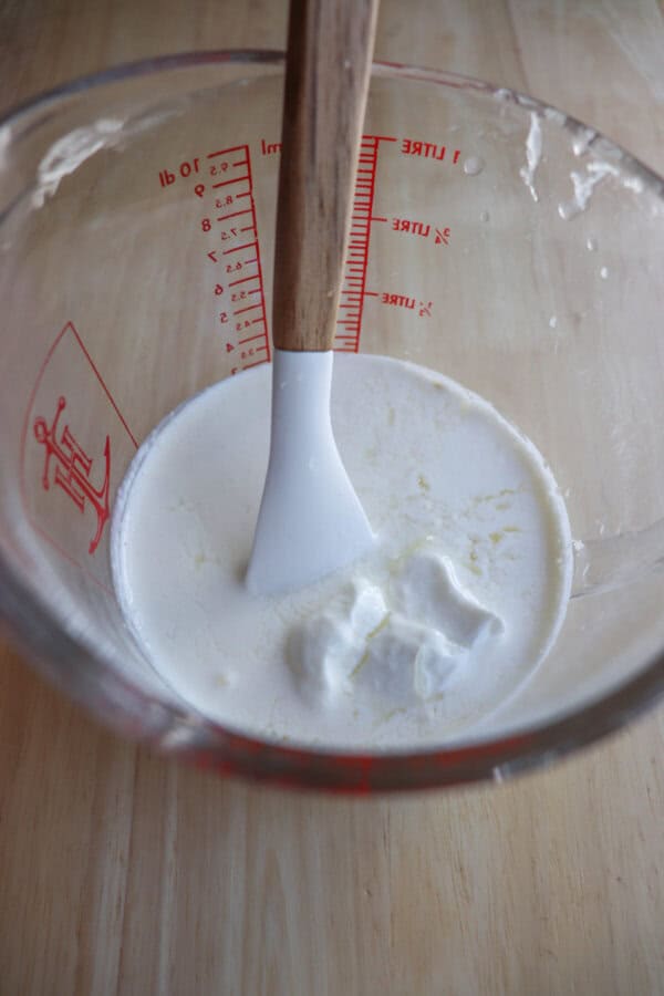 Cream and sour cream in a pyrex mixing cup with a white spatula.