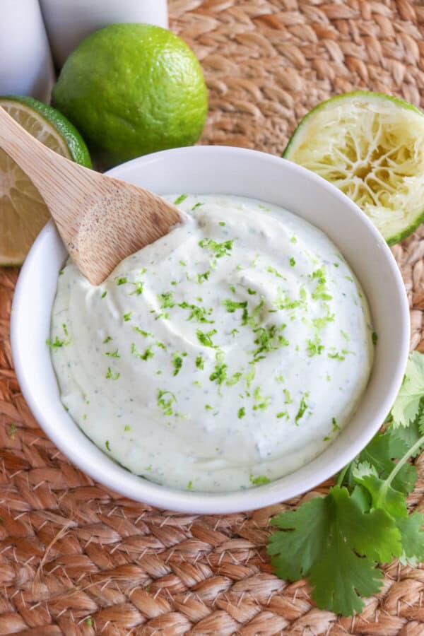 White bowl of crema sauce topped with lime zest with a wooden spoon dipped in on the left.