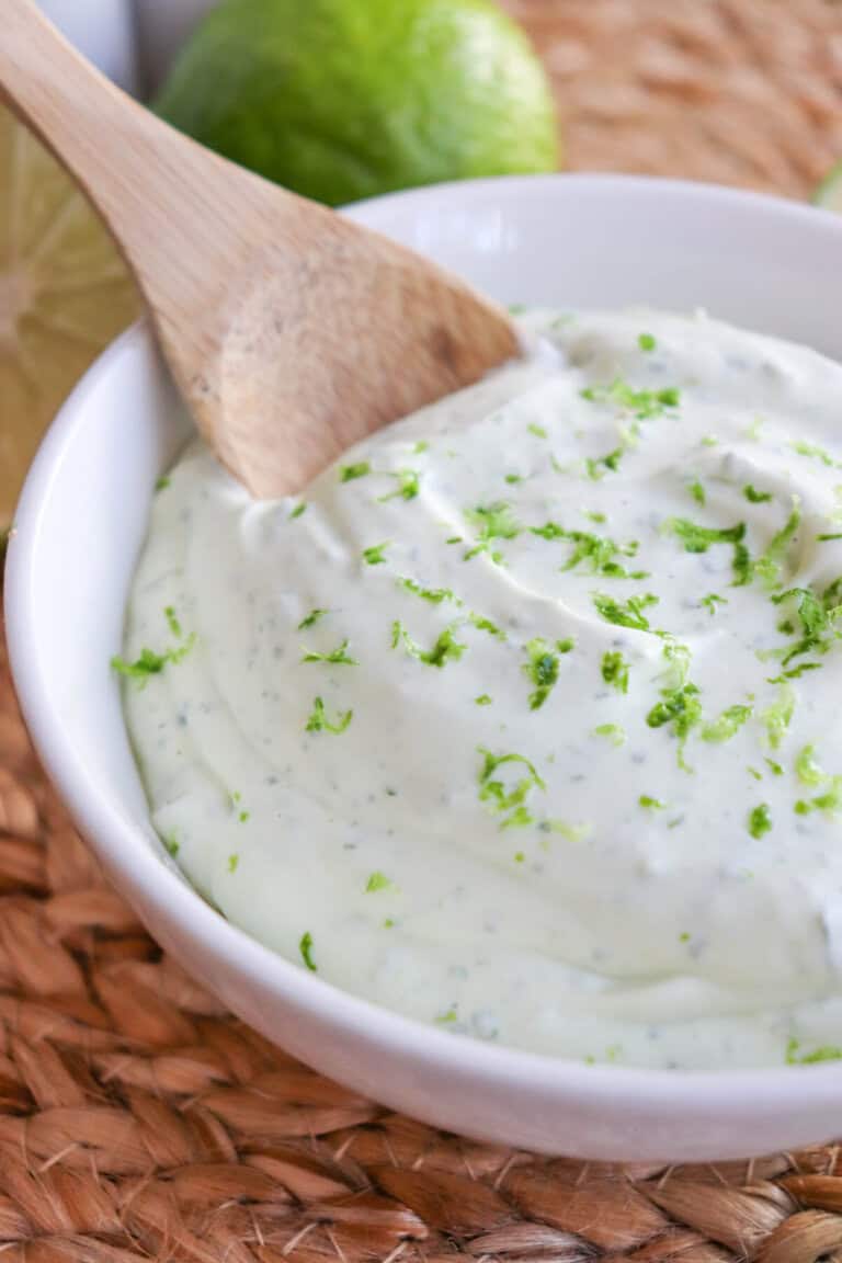 White bowl of crema sauce topped with lime zest with a wooden spoon dipped in on the left.