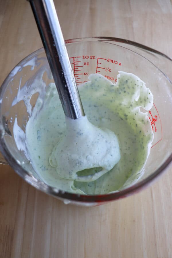 Cilantro lime crema in a pyrex measuring cup with a hand blender in the sauce.