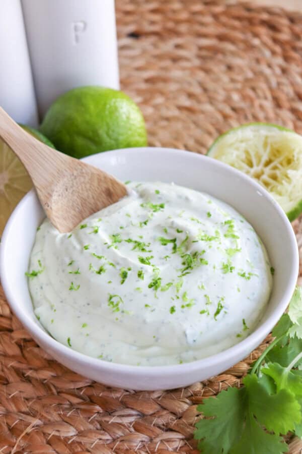White bowl of crema sauce topped with lime zest with a wooden spoon dipped in on the left.