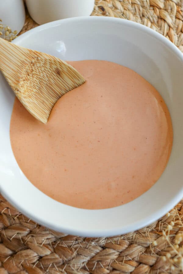 Spicy mayo sauce in a white bowl with a wooden spoon dipped in on the left.