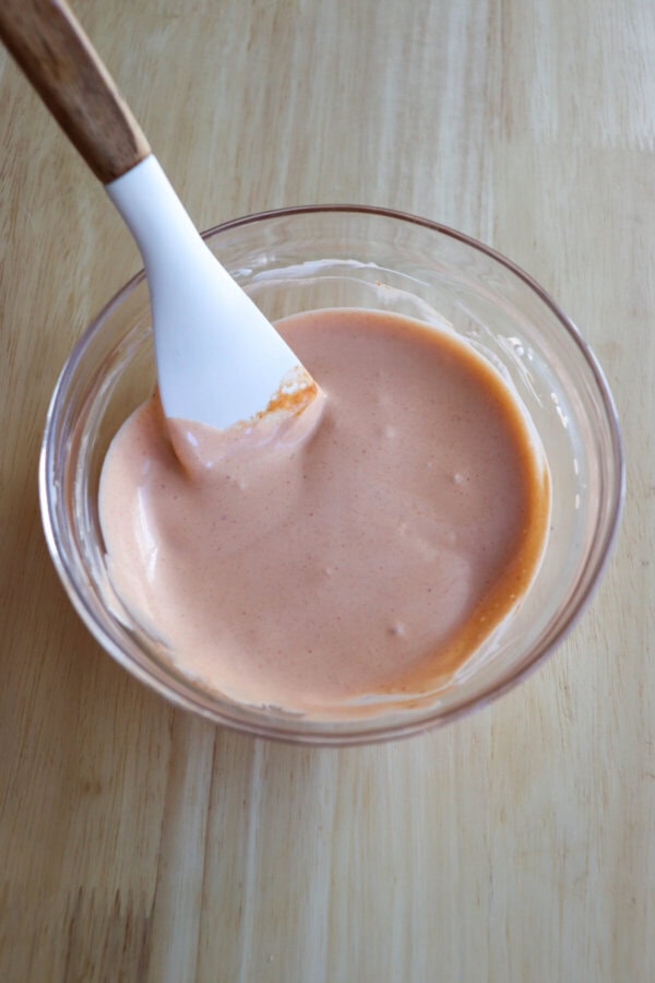 Spicy mayo mixed in a small glass bowl with a spatula.