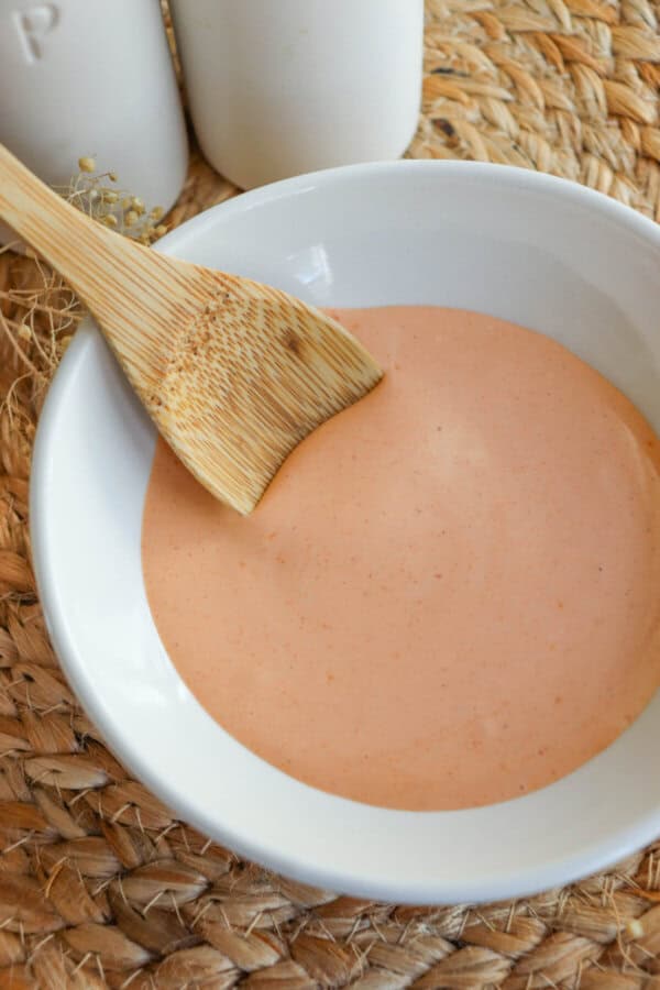 Spicy mayo sauce in a white bowl with a wooden spoon dipped in on the left.