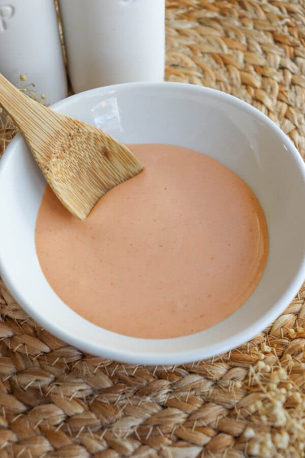 Spicy mayo sauce in a white bowl with a wooden spoon dipped in on the left.