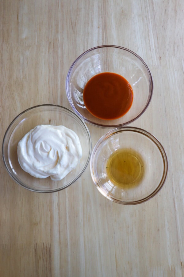 Ingredients for spicy mayo in clear glass bowls on a wooden table.