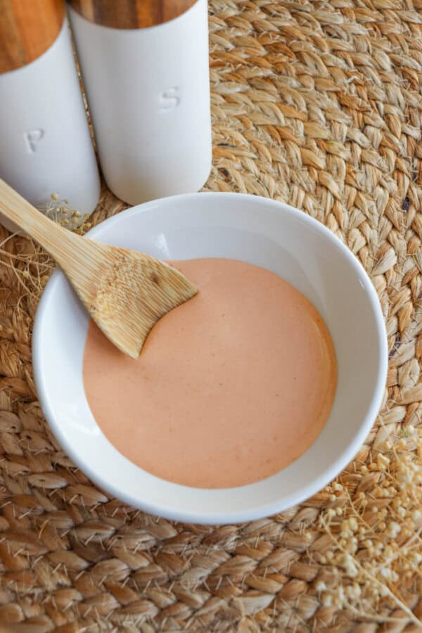 Spicy mayo sauce in a white bowl with a wooden spoon dipped in on the left.