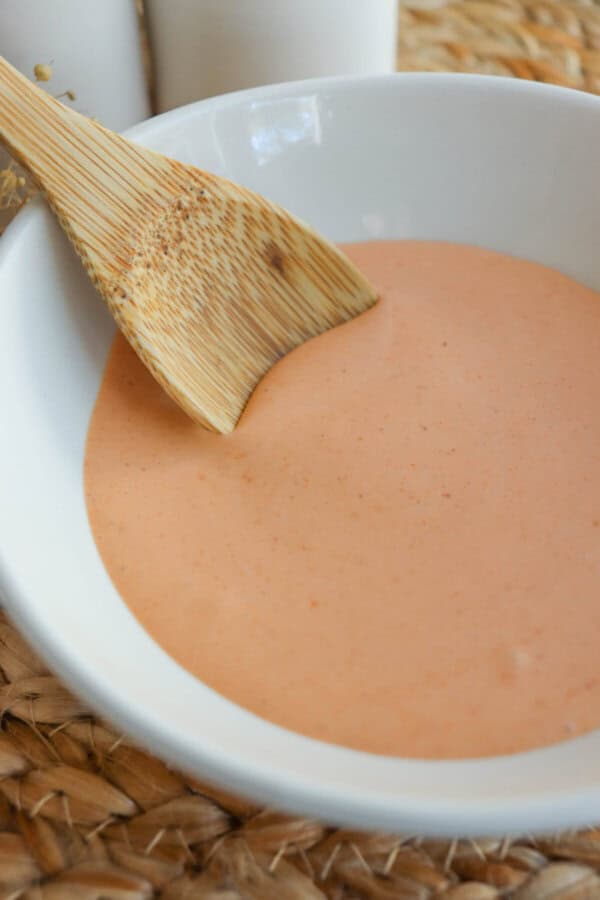 Spicy mayo sauce in a white bowl with a wooden spoon dipped in on the left.