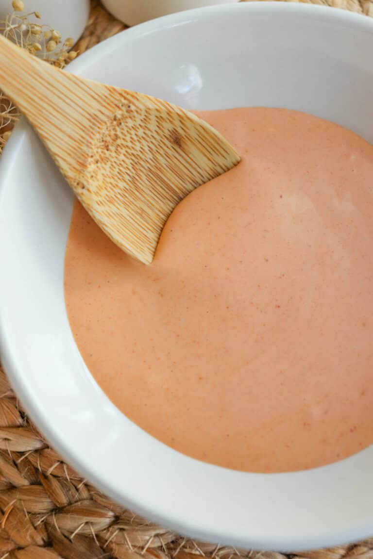 Spicy mayo sauce in a white bowl with a wooden spoon dipped in on the left.