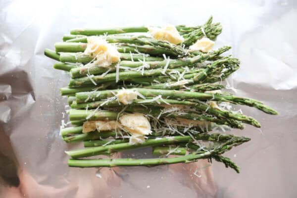 Fresh asparagus on a sheet of foil topped with shredded parmesan and butter.