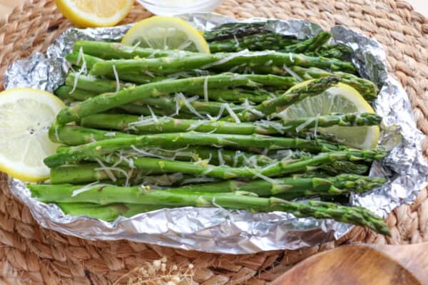 Cooked asparagus in a foil packed topped with shredded parmesan cheese and lemon slices.