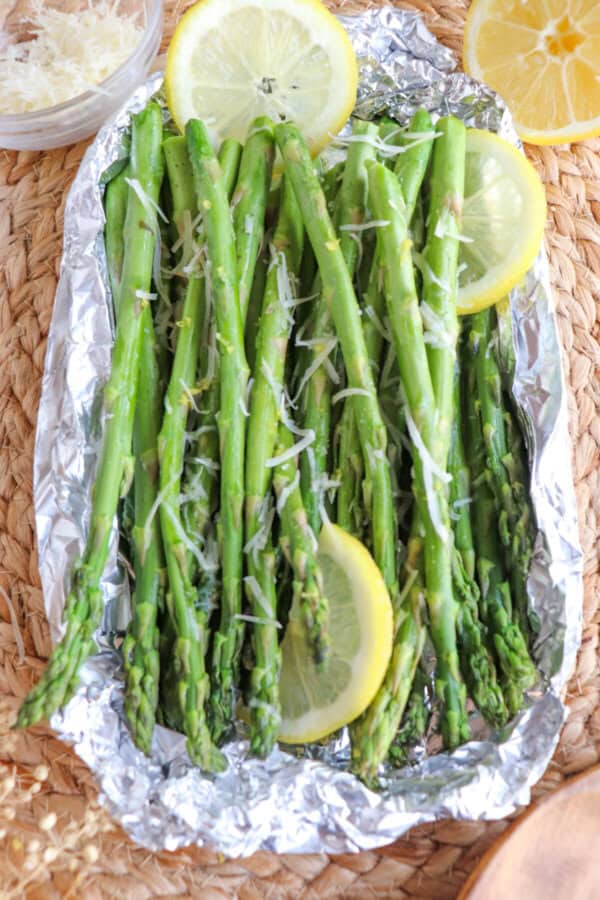 Cooked asparagus in a foil packed topped with shredded parmesan cheese and lemon slices.