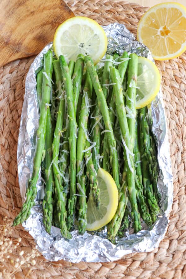 Cooked asparagus in a foil packed topped with shredded parmesan cheese and lemon slices.