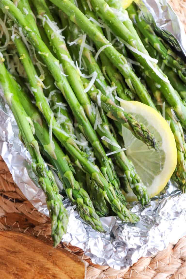 Close up of cooked asparagus in a foil packed topped with shredded parmesan cheese and lemon slices.