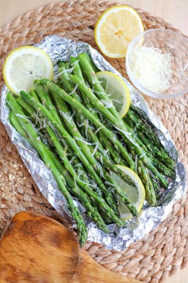 Cooked asparagus in a foil packed topped with shredded parmesan cheese and lemon slices.