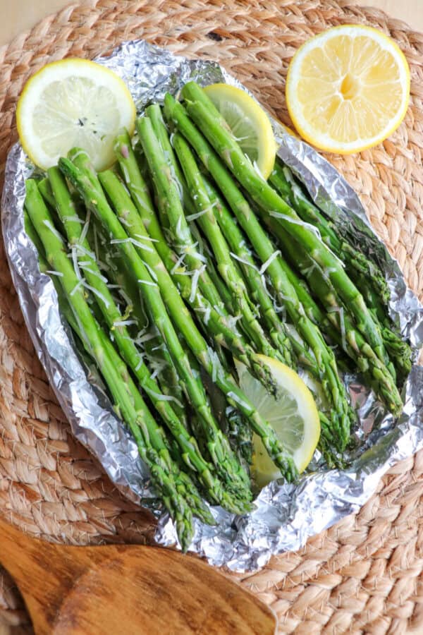 Cooked asparagus in a foil packed topped with shredded parmesan cheese and lemon slices.