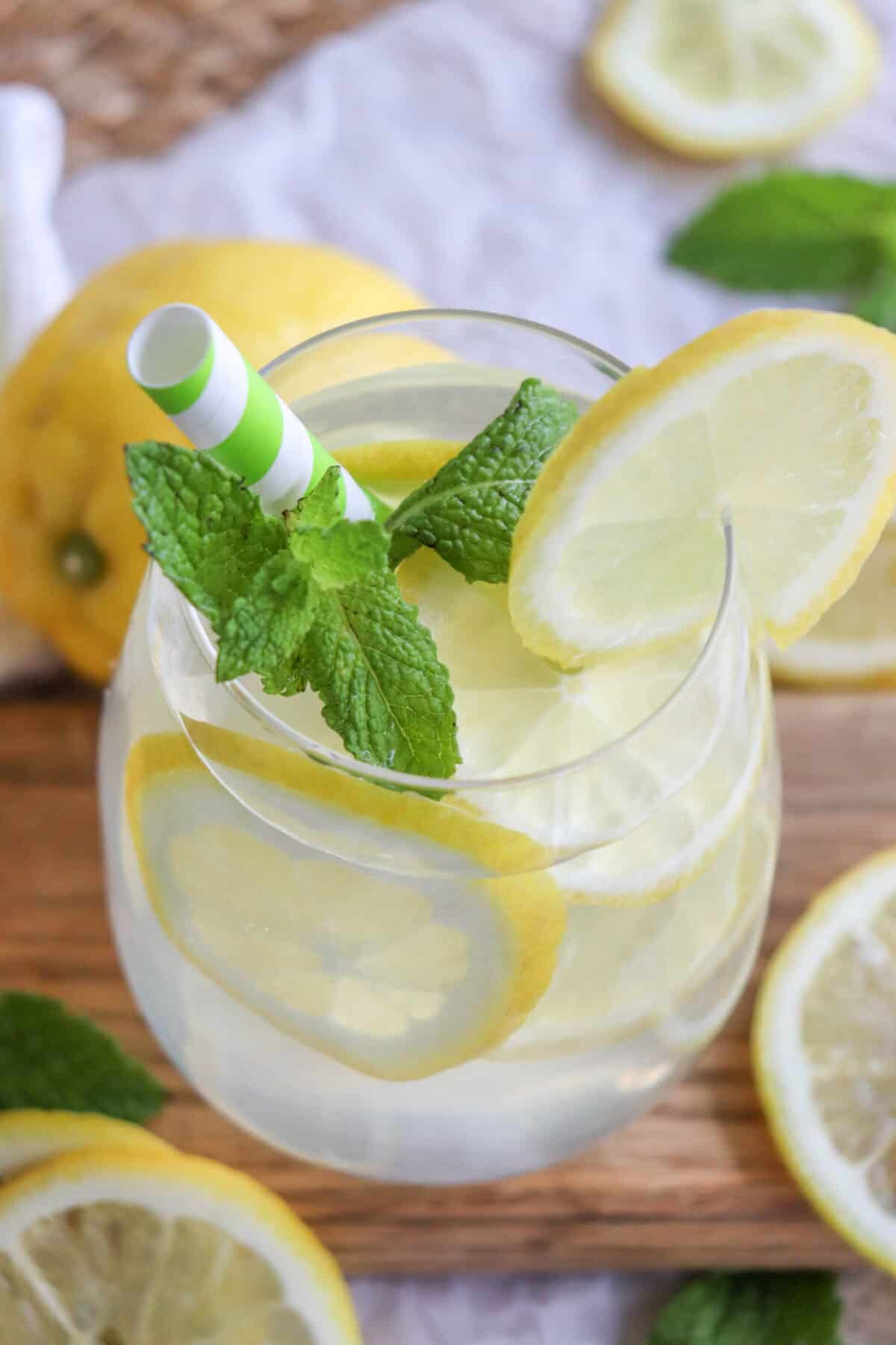 Lemon cocktail in a glass with lemon slices and mint leaves with a green and white straw.