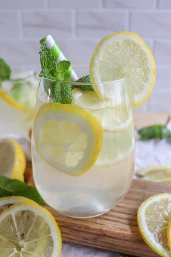 Lemon cocktail in a glass with lemon slices and fresh mint leaves with a green and white straw.