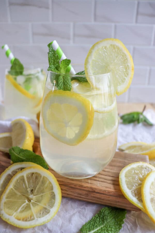 Limoncello cocktail in a glass with lemon slices and mint leaves with a green and white straw.