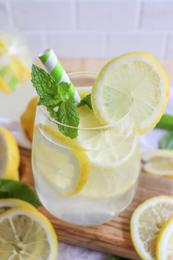 Limoncello cocktail in a glass with lemon slices and mint leaves with a green and white straw.