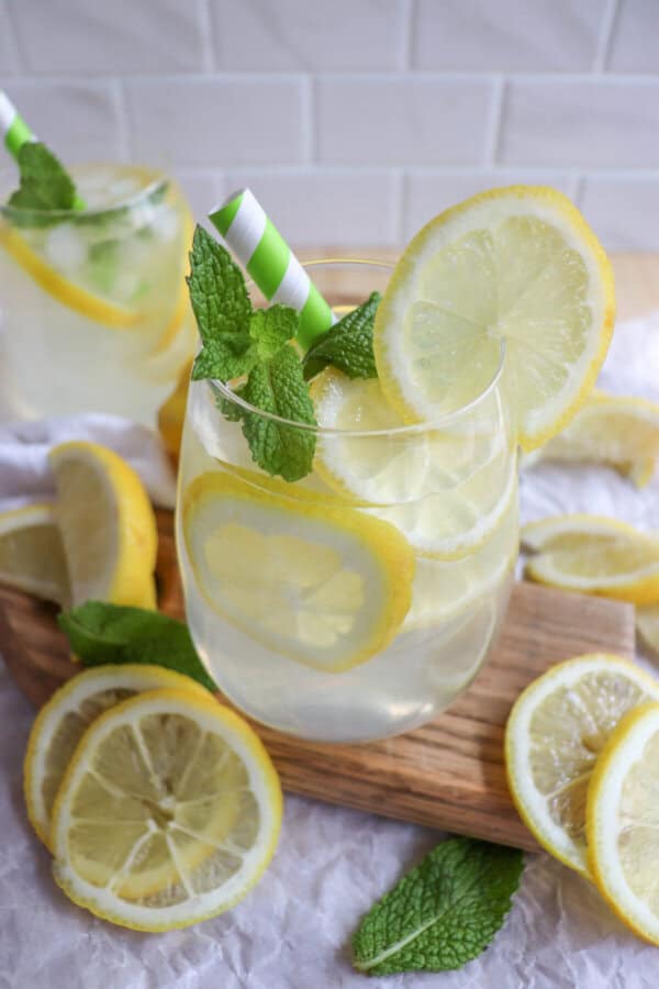 Limoncello cocktail in a glass with lemon slices and mint leaves with a green and white straw.